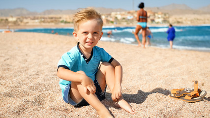 Portrait of adorable toddler boy enjoying sitting on the beach at sea