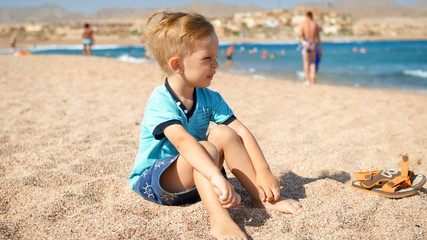 Portrait of upset toddler boy sitting on sand at sea beach