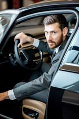 Portrait of a handsome businessman sitting on the driver seat of a luxury car in the showroom