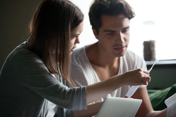 Fototapeta premium Close up stressed millennial couple sitting on sofa at home and check unpaid bills, taxes, due debt and bank account balance. Bankruptcy, debt and lack of money, financial problems in family concept