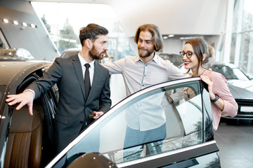 Car salesman showing car interior to a young couple clients in the showroom