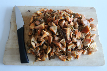 Minced saffron milk cap mushrooms (Lactarius deliciosus) caps, similar to Sanguifluus and Deterrimus, on a wooden cutting board with a knife