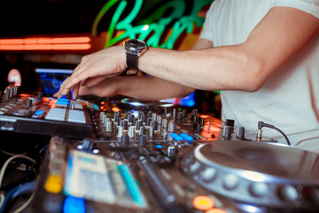 Dj mixes the track in the nightclub at party. Headphones in foreground and DJ hands in motion