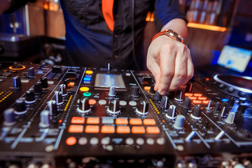 Dj mixes the track in the nightclub at party. Headphones in foreground and DJ hands in motion