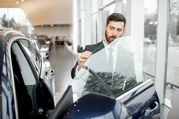 Businessman looking on the frameless window of a luxury car in the showroom
