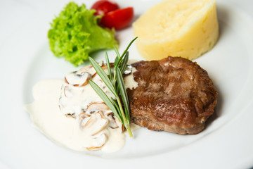 Juicy fresh roasted steak with champignons and mashed potatoes. Decorated with lettuce, cherry tomatoes and rosemary. Served with white sauce.