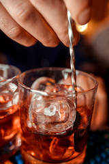 Bartender finishes preparation of orange alcoholic cocktail in crystal glass by adding a bitter of powdered sugar. Close-up of expert bartender making cocktail in bar.