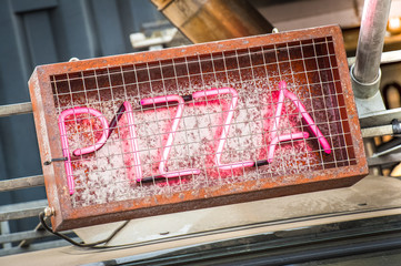 neon pizza sign in a rusting metal cage