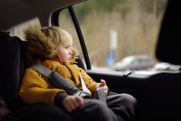 Portrait of pretty little boy sitting in car seat during roadtrip or travel. Family car travel with kids.
