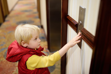 Little boy presses the button to call the elevator in the hotel lobby
