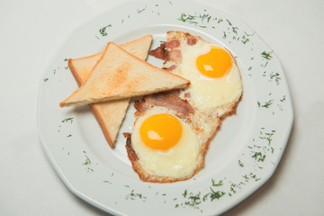 Appetizing fried eggs on white plate with toasts and bacon decorated with greenery. Nutritious breakfast. 