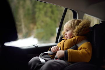 Portrait of pretty little boy sitting in car seat during roadtrip or travel. Family car travel with kids.
