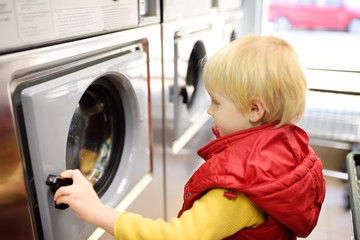 A little boy loads clothes into the washing machine in public laundrette