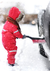 Cute little child helping to brush a snow from a car