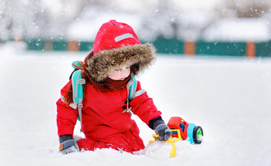 Little boy playing with bright car toy and fresh snow