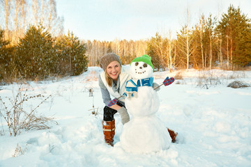 happy woman playing with snowman in the winter outdoors