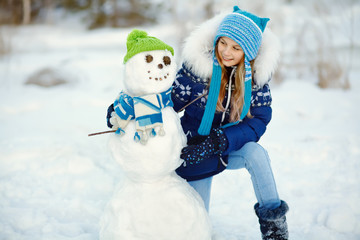 happy kid playing with snowman in the winter outdoors