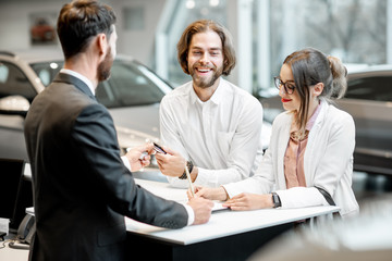 Young business couple signing some documents at the table with salesperson or manager buying or...