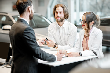 Young business couple signing some documents at the table with salesperson or manager buying or...