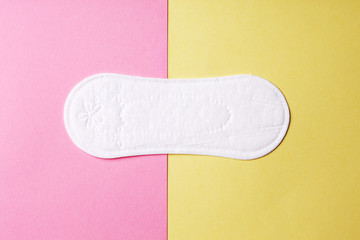 soft clean cotton menstruation pad lying on pink and yellow background, modern pastel colors, top view