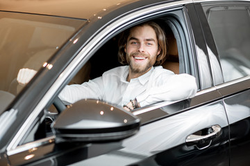 Portrait of a happy owner sitting on a driver seat of a new luxury car at the showroom