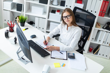 Young girl sitting at the table and working with a computer, documents and calculator