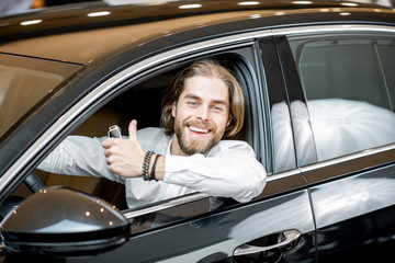 Portrait of a happy owner sitting on a driver seat of a new luxury car at the showroom