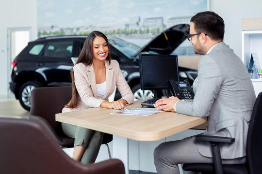 Potential female vehicle buyer carefully listening to car dealer you car that are in salon.