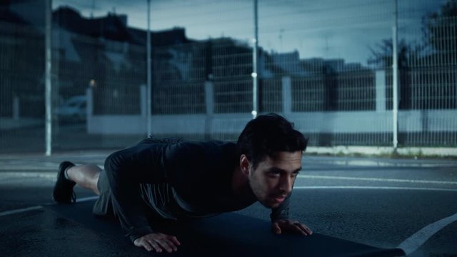 Strong Muscular Fit Young Man in Sport Outfit Doing Push Up Exercises. He is Doing a Workout in a Fenced Outdoor Basketball Court. Evening Footage After Rain in a Residential Neighborhood Area.