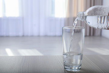 Pouring water from bottle into glass on blurred background. Space for text