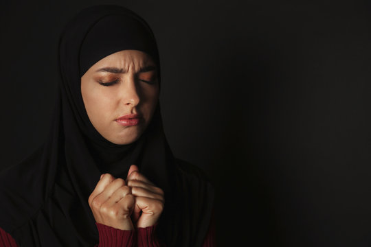 Portrait Of Sad Muslim Woman In Hijab  Praying On Dark Background. Space For Text