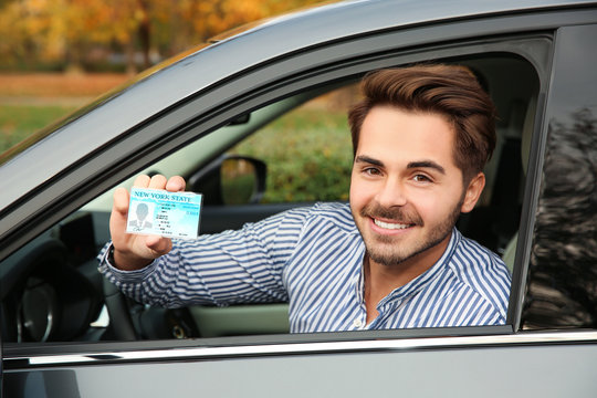 Young man holding driving license in car