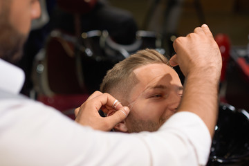Barber doing threading procedure of eyebrows in barbershop