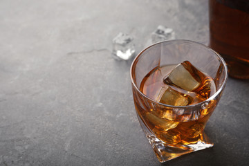 Golden whiskey in glass with ice cubes on table. Space for text