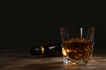 Golden whiskey in glass with ice cubes on table. Space for text