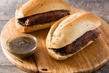 Choripan. Traditional Argentina sandwich with chorizo and chimichurri sauce on wooden table