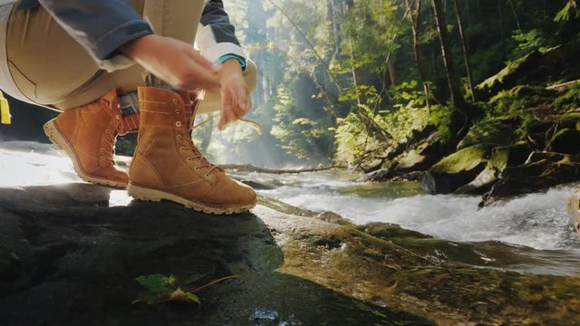 The tourist ties up his shoelaces on his shoes. In the forest near a mountain stream