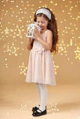 girl child is posing with lantern in christmas lights, yellow background, pink dress