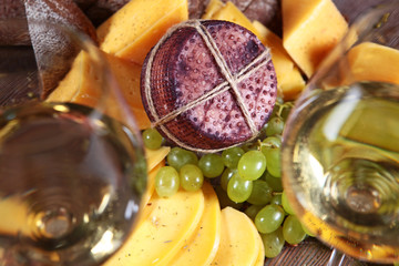 Home-made cheese and two glasses of white wine are out of focus. Green grapes next to cheese. Still life on a wooden background. The concept of still life.