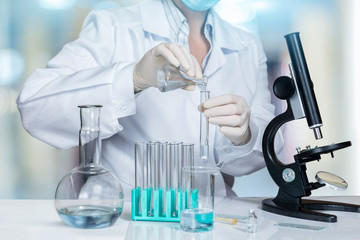 A laboratory assistant is making some experiments with a microscope and substances in test tubes and flasks.