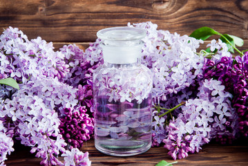 Obraz na płótnie Canvas Fresh lilac flower petals floating on water in a glass jar on a dark wooden background