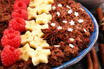 Bowl of cacao oatmeal porridge with banana, raspberries coconut and caramel sauce on rustic table, hot and healthy food for Breakfast