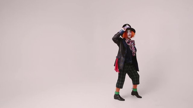 an actor in a hatter costume, he jumps and smiles. At white studio