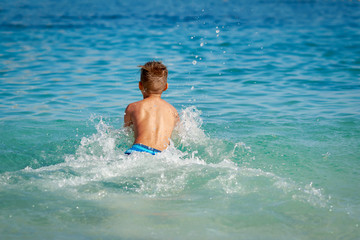 Cute European boy in a striped swimming pants spending his holidays at the sea. He is swimming in the water making a lots of splashes around.