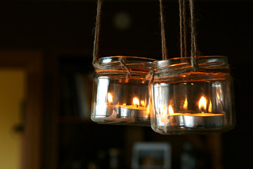 Aromatic candles in jars hanging in interior. DIY candles in glass jars hanging on linen jute. 