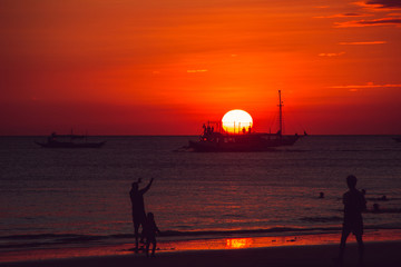Dramatic orange sea sunset with sailboat and people silhouettes. Summer time. Travel to Philippines. Luxury tropical vacation. Boracay paradise island. Seascape view. Tourism concept. Water transport