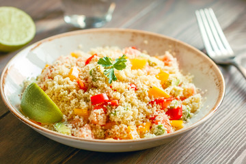 Couscous salad with fresh red and yellow bell peppers, avocado, tomatoes and lime. The concept of vegetarian and healthy food.