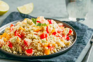 Couscous salad with fresh red and yellow bell peppers, avocado, tomatoes and lime. The concept of vegetarian and healthy food.