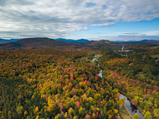 Naklejka premium Low level aerial photograph featuring fall foliage in the Adirondack Park of New York State featuring peak fall foliage colors near Saranac Lake, NY and the Saranac River.