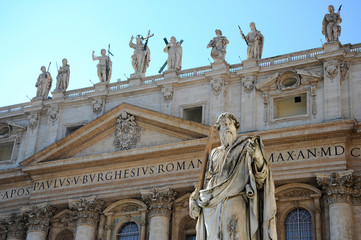 Statue of Apostle Paul in front of the St Peter's Basilica, Vatican City (Rome, Italy). Detail of the facade exterior on the blue sky background. The Apostle Paul with a sword in sunlight.